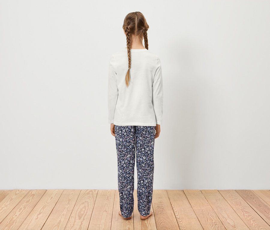 Dievča s dvoma vrkočmi stojí chrbtom k fotoaparátu, má na sebe biele tričko s dlhým rukávom a kvetinové nohavice.