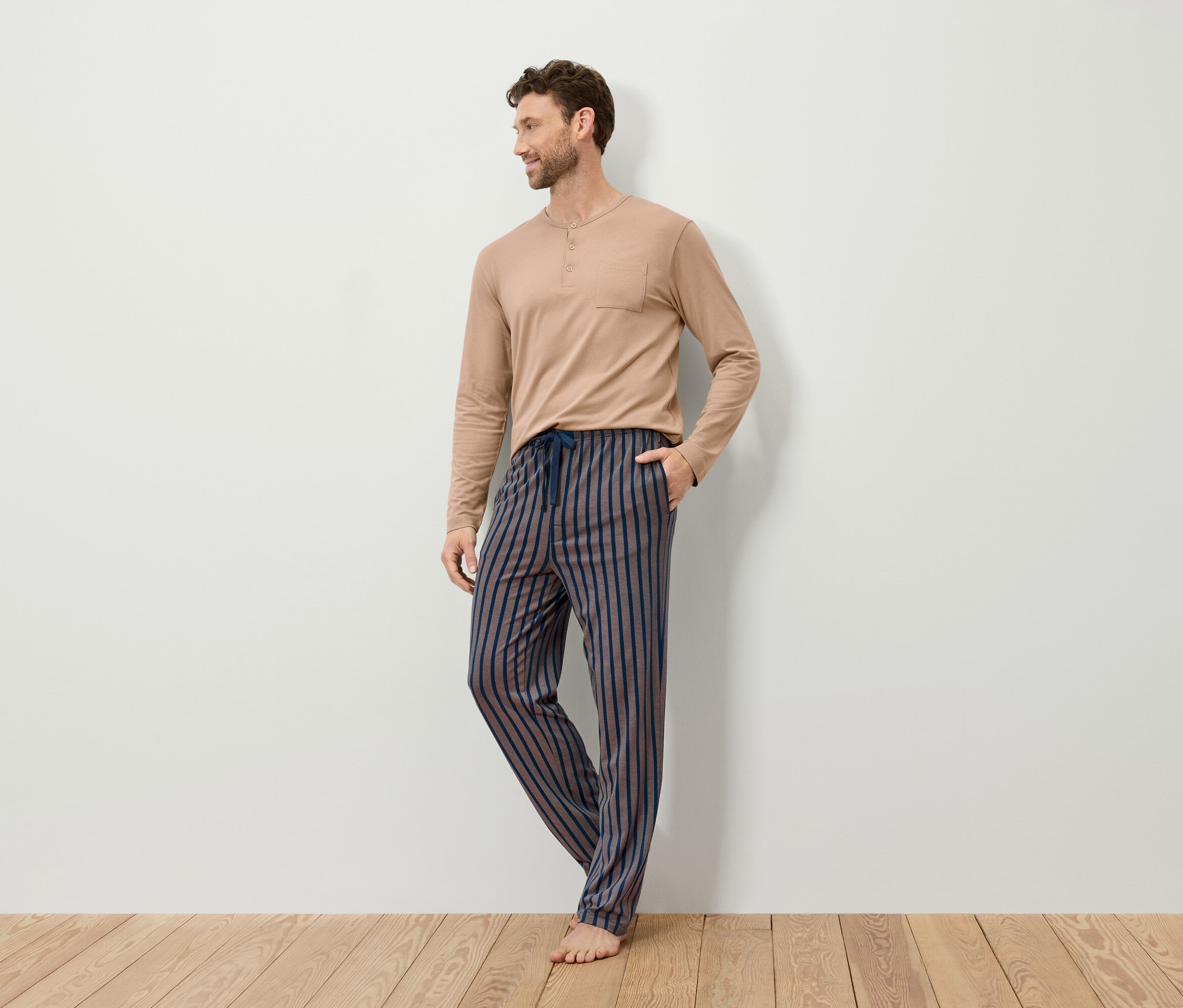 Muž v béžovom pyžamovom tope s dlhým rukávom a pruhovaných pyžamových nohaviciach.