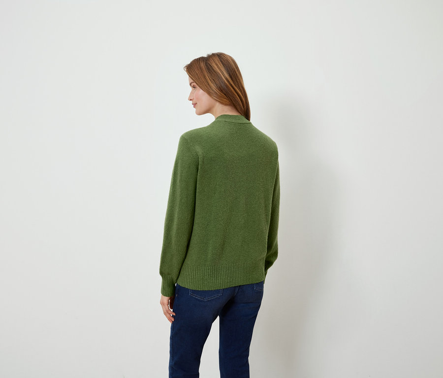 Žena sa pozerá cez plece a má na sebe zelený sveter a džínsy.