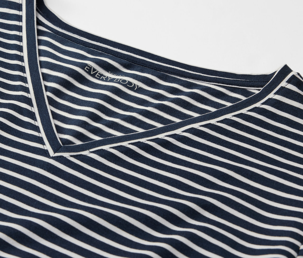 Detail modrého trička s bielymi pruhmi a véčkovým výstrihom.
