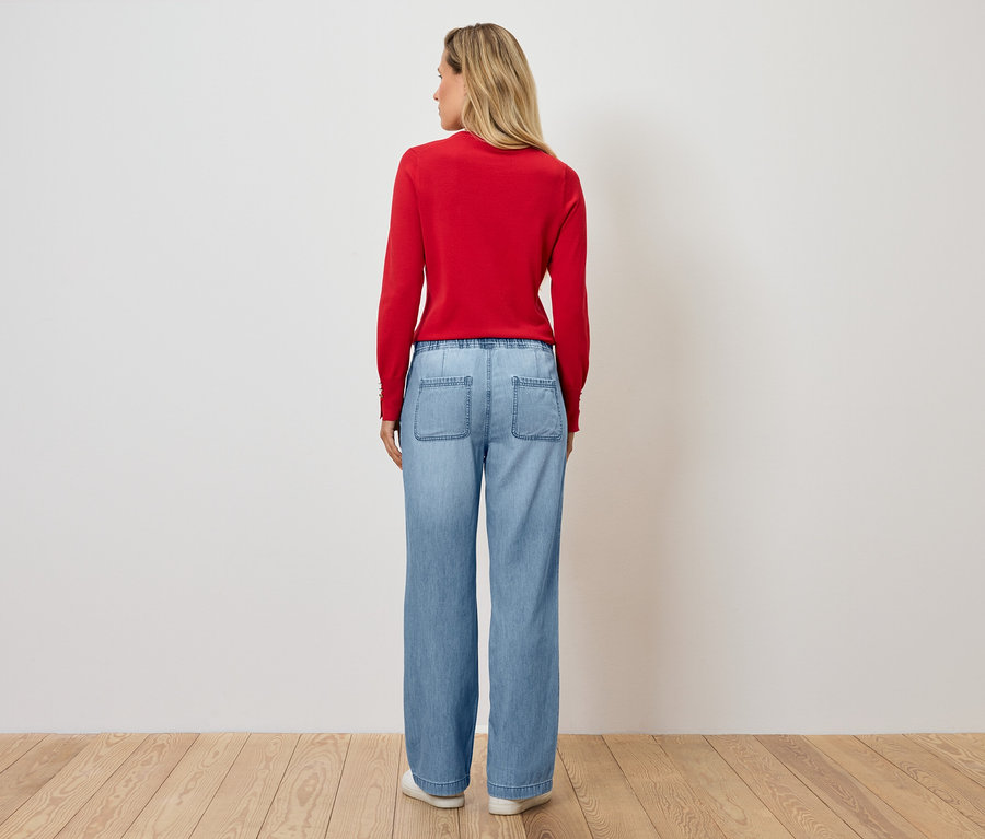 Žena stojí chrbtom k fotoaparátu a má na sebe červený sveter a modré džínsy.