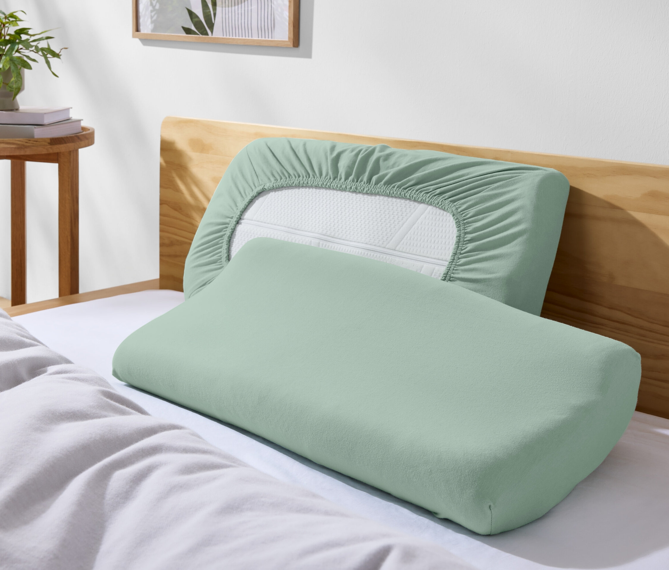 Dva zelené vankúše na posteli s bielymi obliečkami.