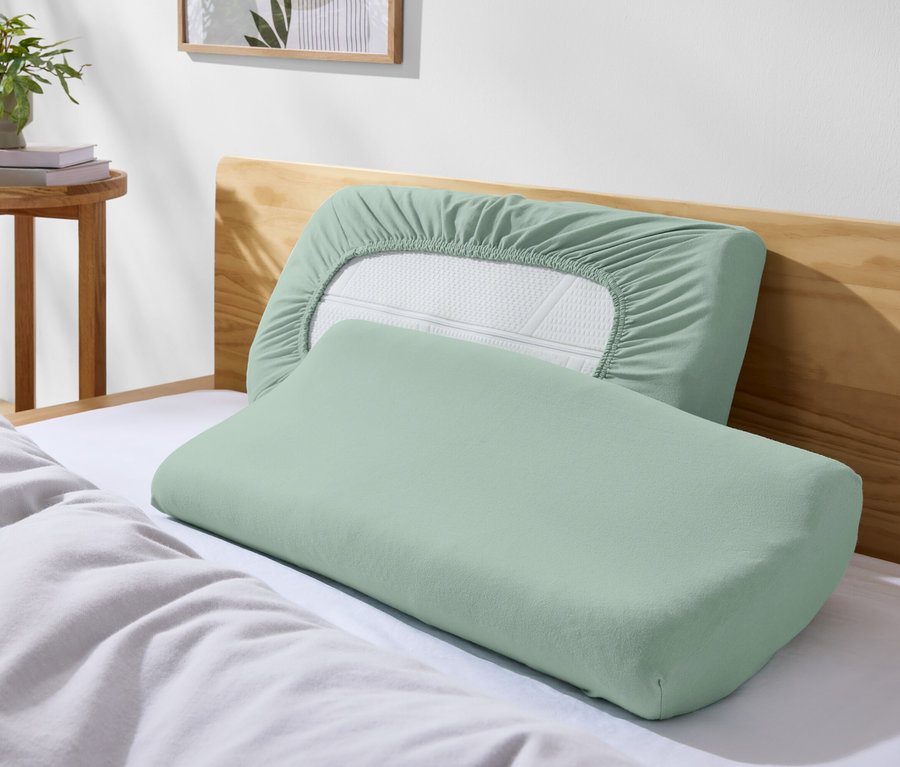 Dva zelené vankúše na posteli s bielymi obliečkami.