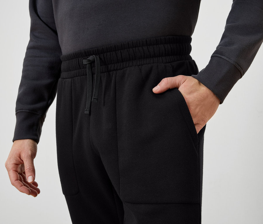 Muž má ruku vo vrecku čiernych teplákov.