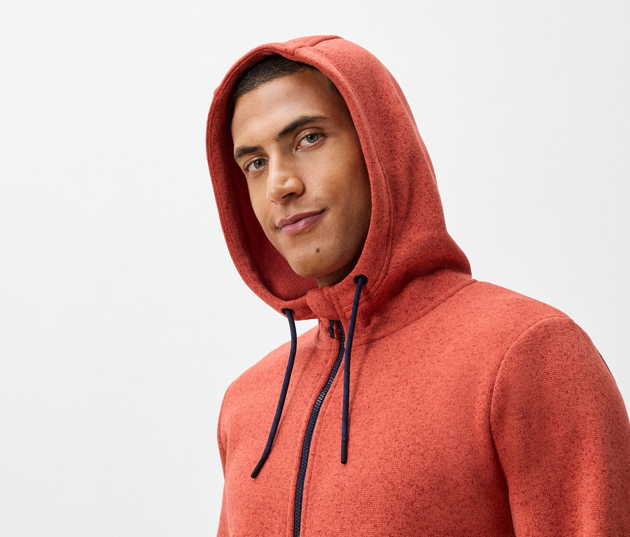Portrét muža s kapucňou a tmavomodrým zipsom na oranžovej mikine.