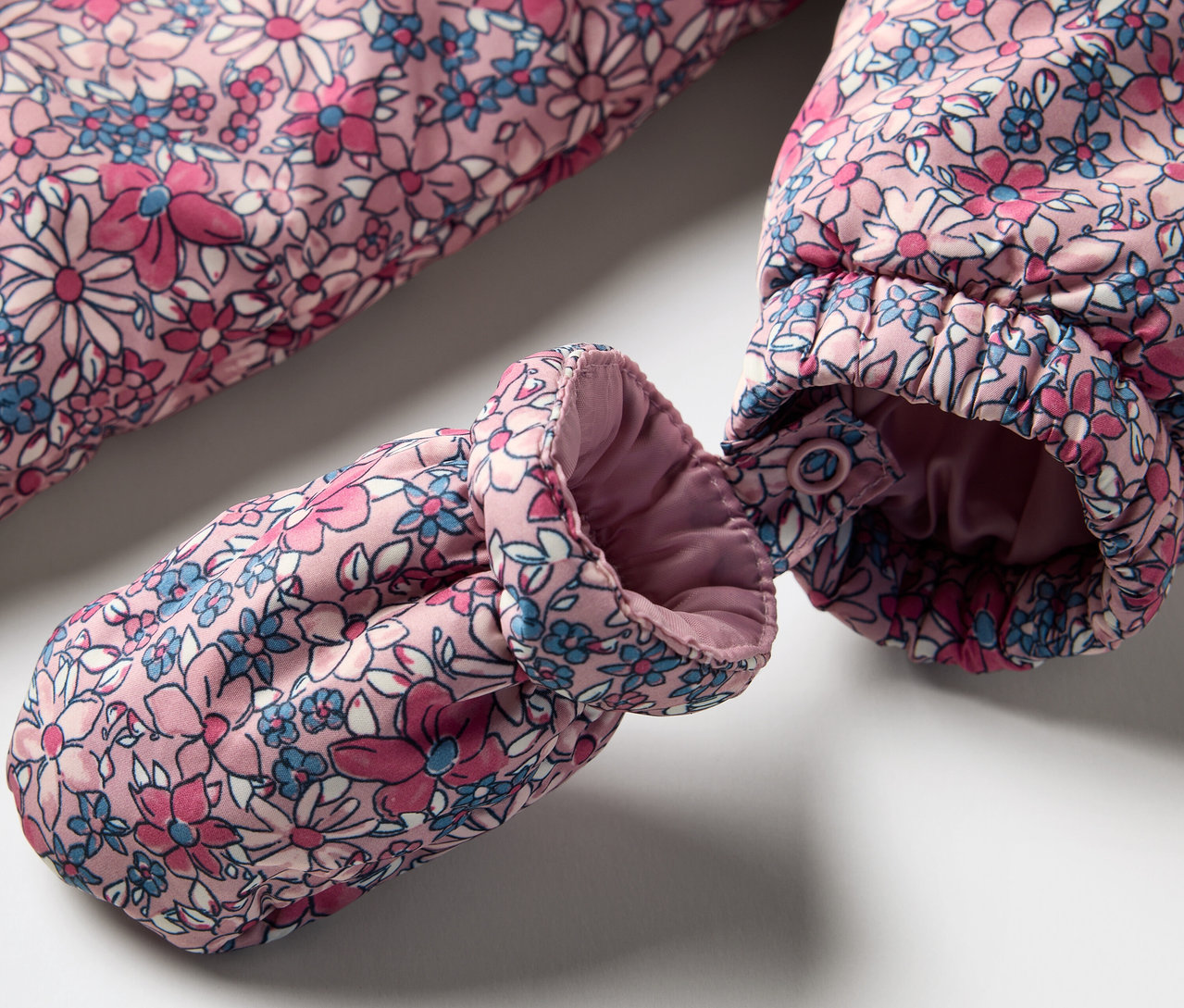 Detail zimného overalu pre bábätká s kvetinovým vzorom a rukavicou.