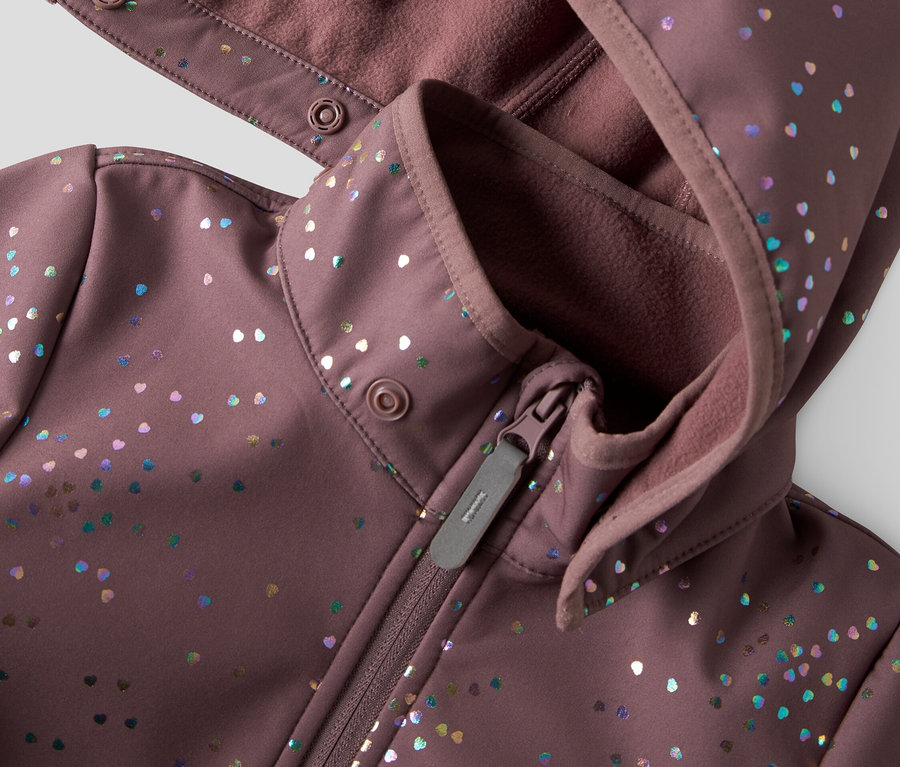Detail fialovej softshellovej bundy s kapucňou a zipsom, zdobenej farebnými bodkami v tvare srdca.