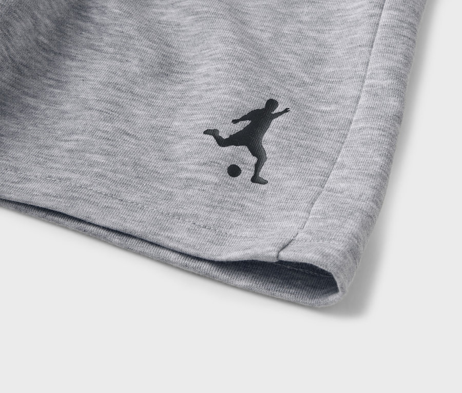 Detail šedých šortiek s čiernou siluetou futbalistu.