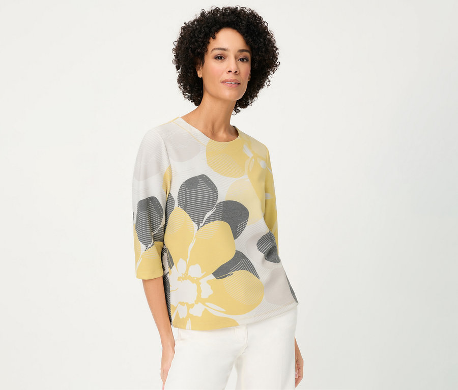 Žena nosí mikinu Olsen »Ottoman« so žltými a sivými kvetmi na bielom pozadí.