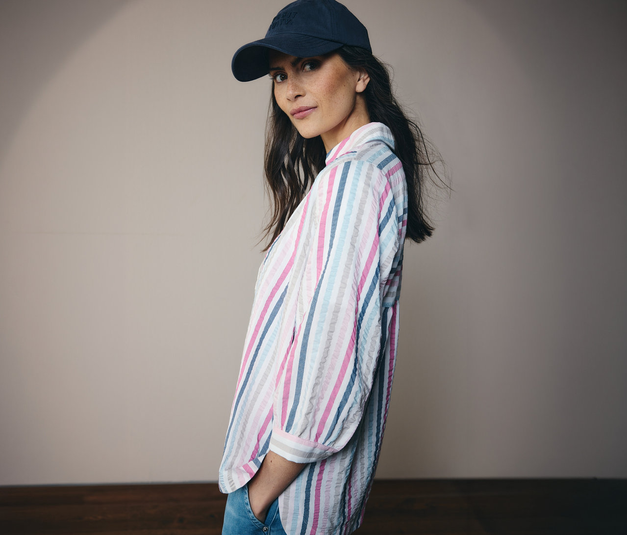 Žena v modrej čiapke a pásikavá košeľová blúzka CECIL sa pozerá do kamery.