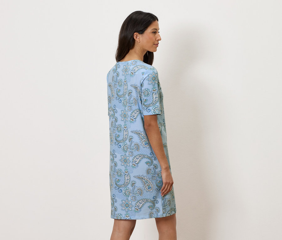 Žena stojí bokom a má na sebe svetlomodré kvetinové šaty.