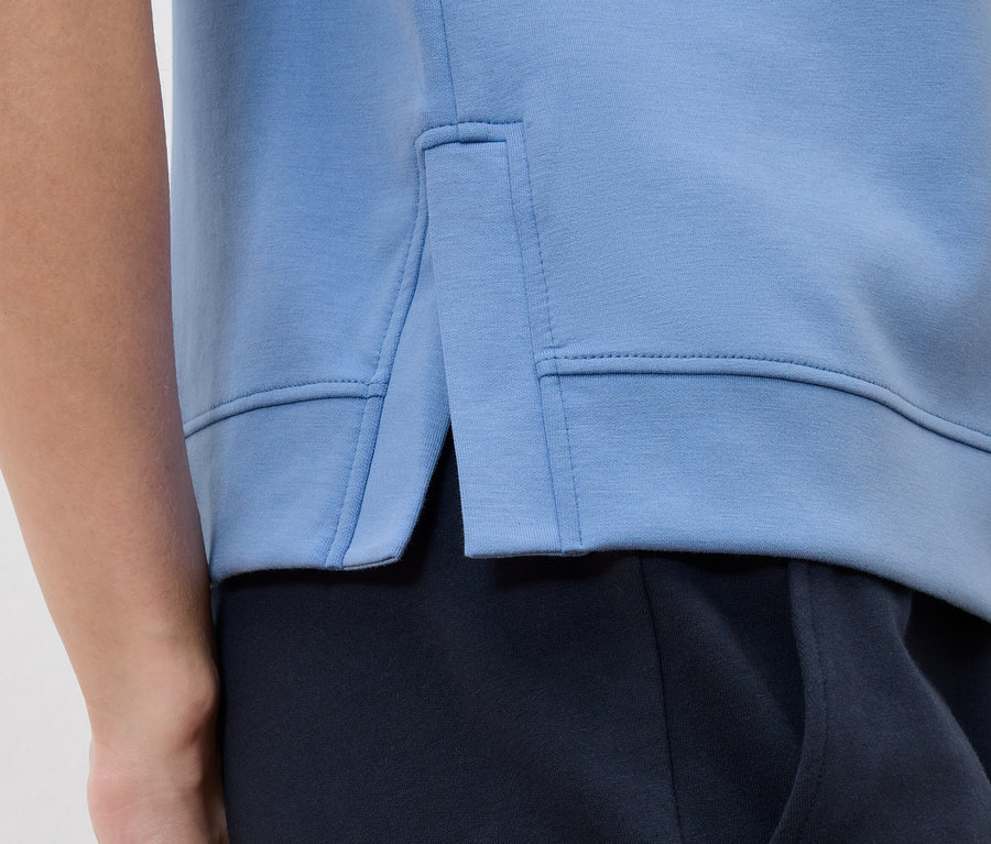 Detailný záber svetlomodrej mikiny s bočným rozparkom cez tmavomodré nohavice.