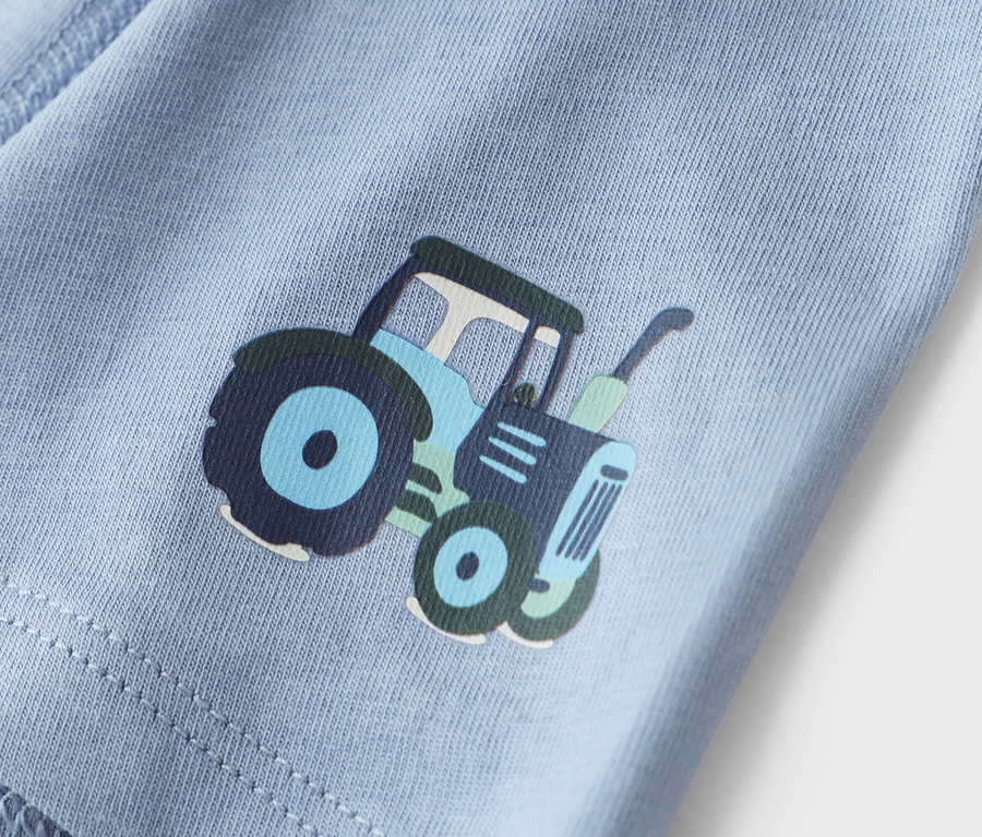 Detailný záber svetlomodrej látky s potlačou traktora.