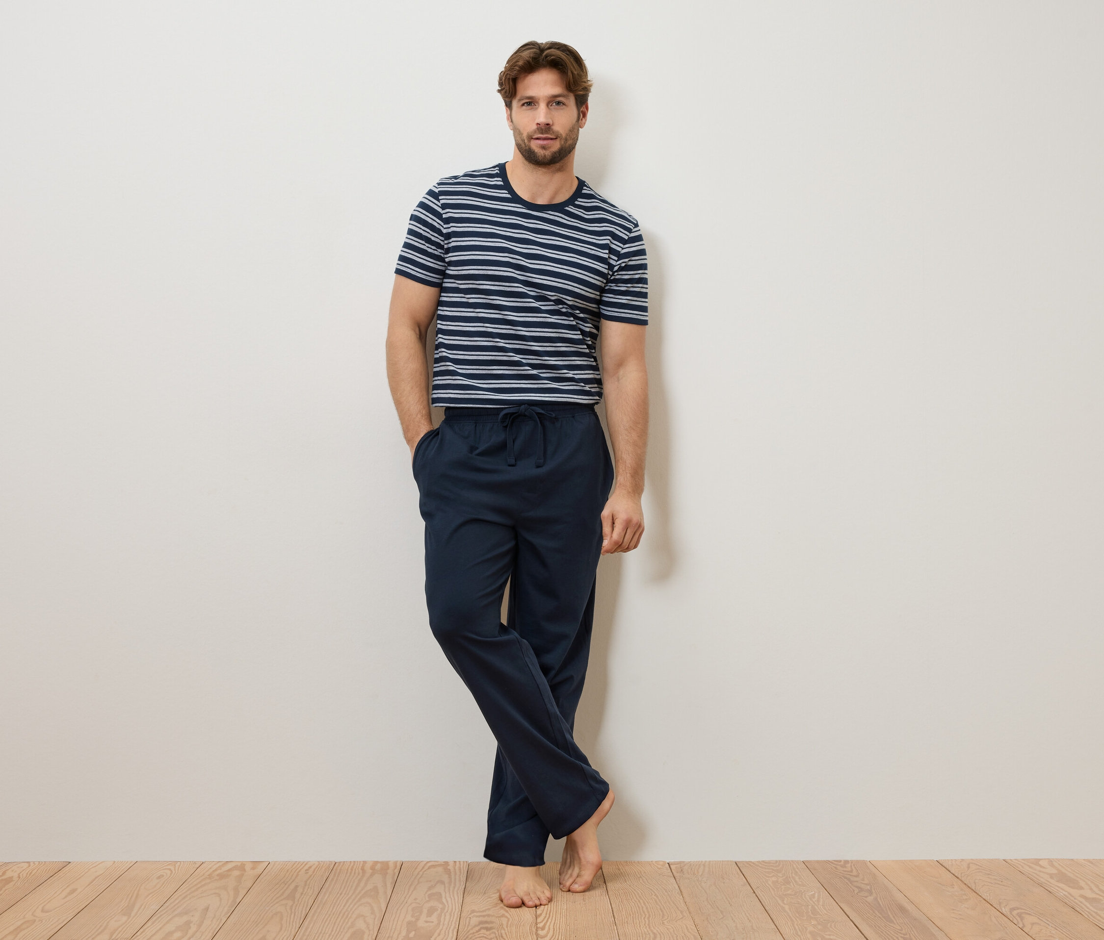 Muž sa opiera o stenu, má na sebe modro-biele pruhované tričko a tmavomodré pyžamové nohavice.