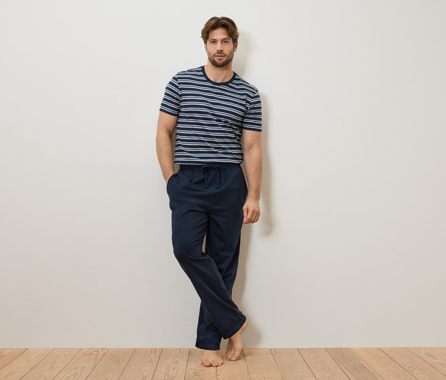Muž sa opiera o stenu, má na sebe modro-biele pruhované tričko a tmavomodré pyžamové nohavice.