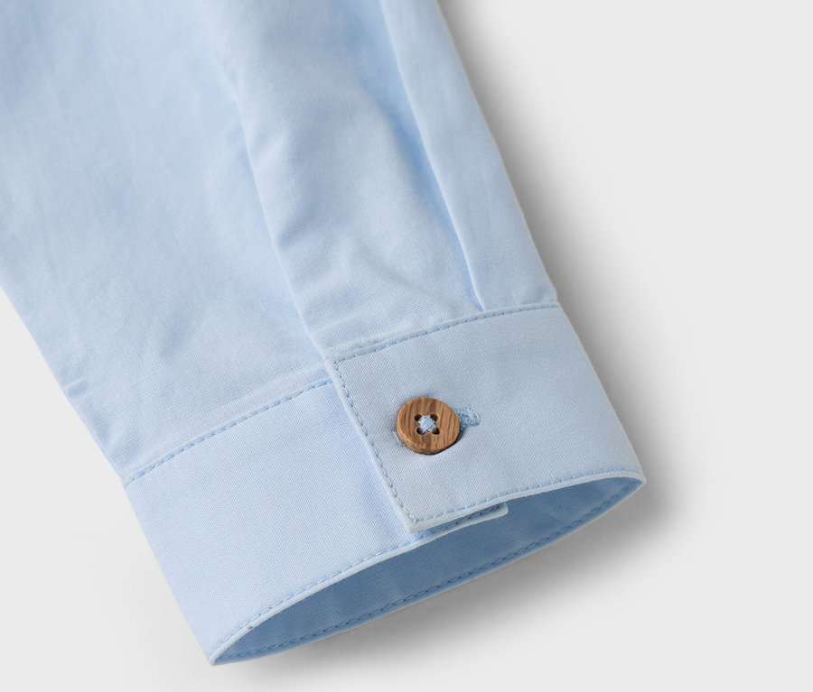 Detail záberu rukáva svetlomodrej košele s hnedým gombíkom.