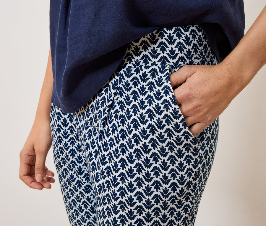 Zblízka osoba v námorníckych vzorovaných nohaviciach a námorníckom vrchnom diele s rukou vo vrecku nohavíc.