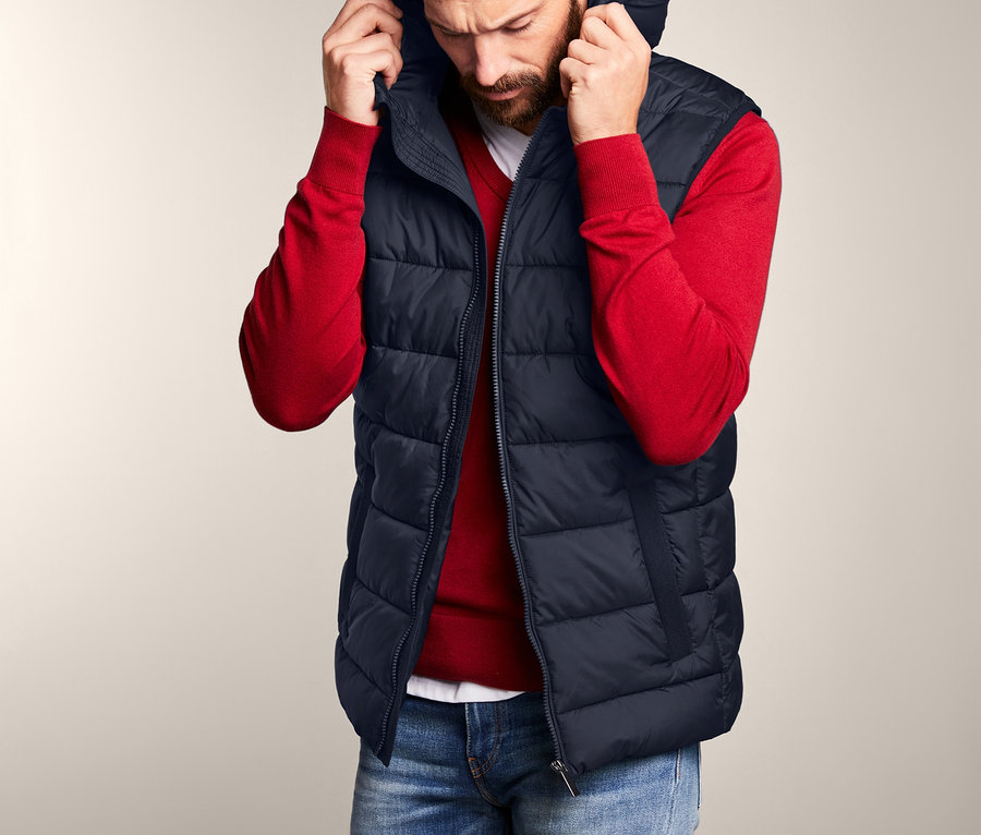 Muž si upravuje kapucňu prešívanej vesty s kapucňou.