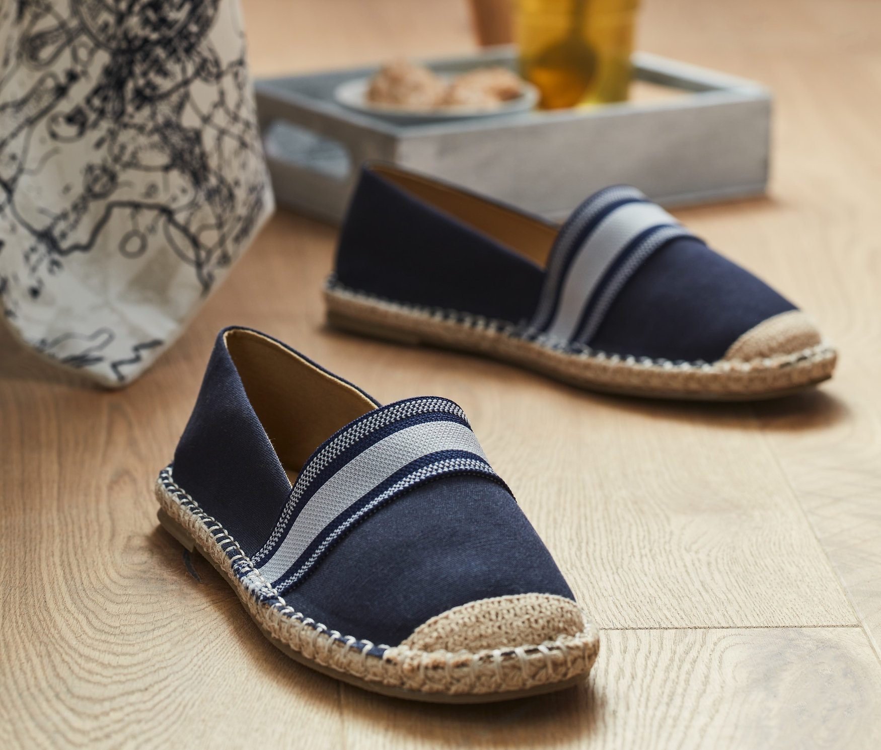 Dvoje espadrilky na drevenej podlahe blízko pohára s nápojom.