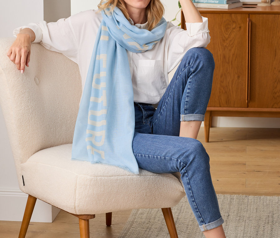 Žena sedí v kresle a má na sebe tkaný šál so statement potlačou.