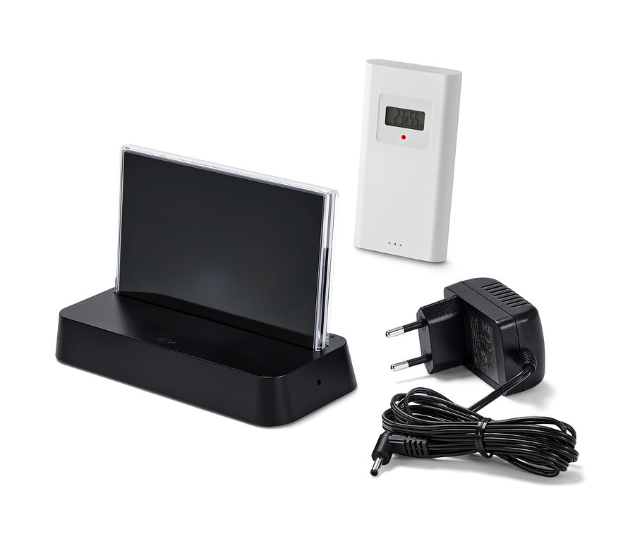 Čierna meteorologická stanica riadená rádiovým signálom s farebným LCD displejom, bielym senzorom a čiernym napájacím adaptérom na bielom pozadí.