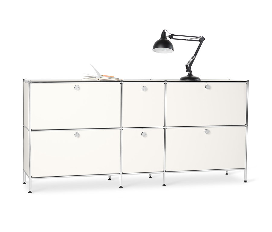 Biela kovová odkladacia skrinka »CN3« so 6 výklopnými priehradkami. Na vrchu leží otvorený zápisník a stojí čierna lampa.