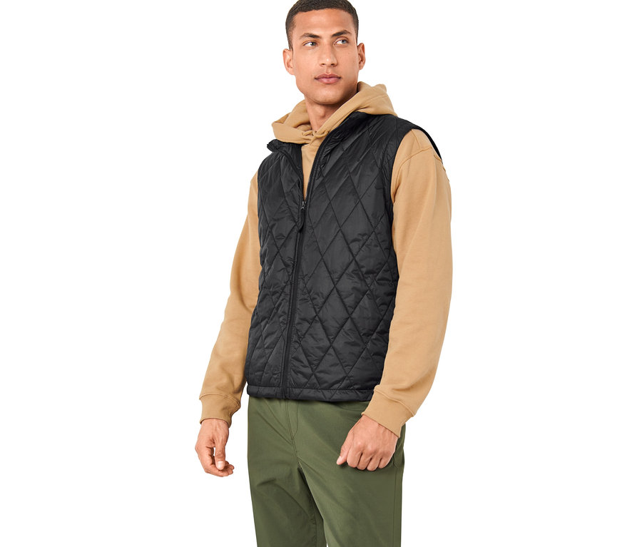 Muž má na sebe čiernu vestu z outdoorovej bundy 3 v 1 a olivovozelené nohavice.