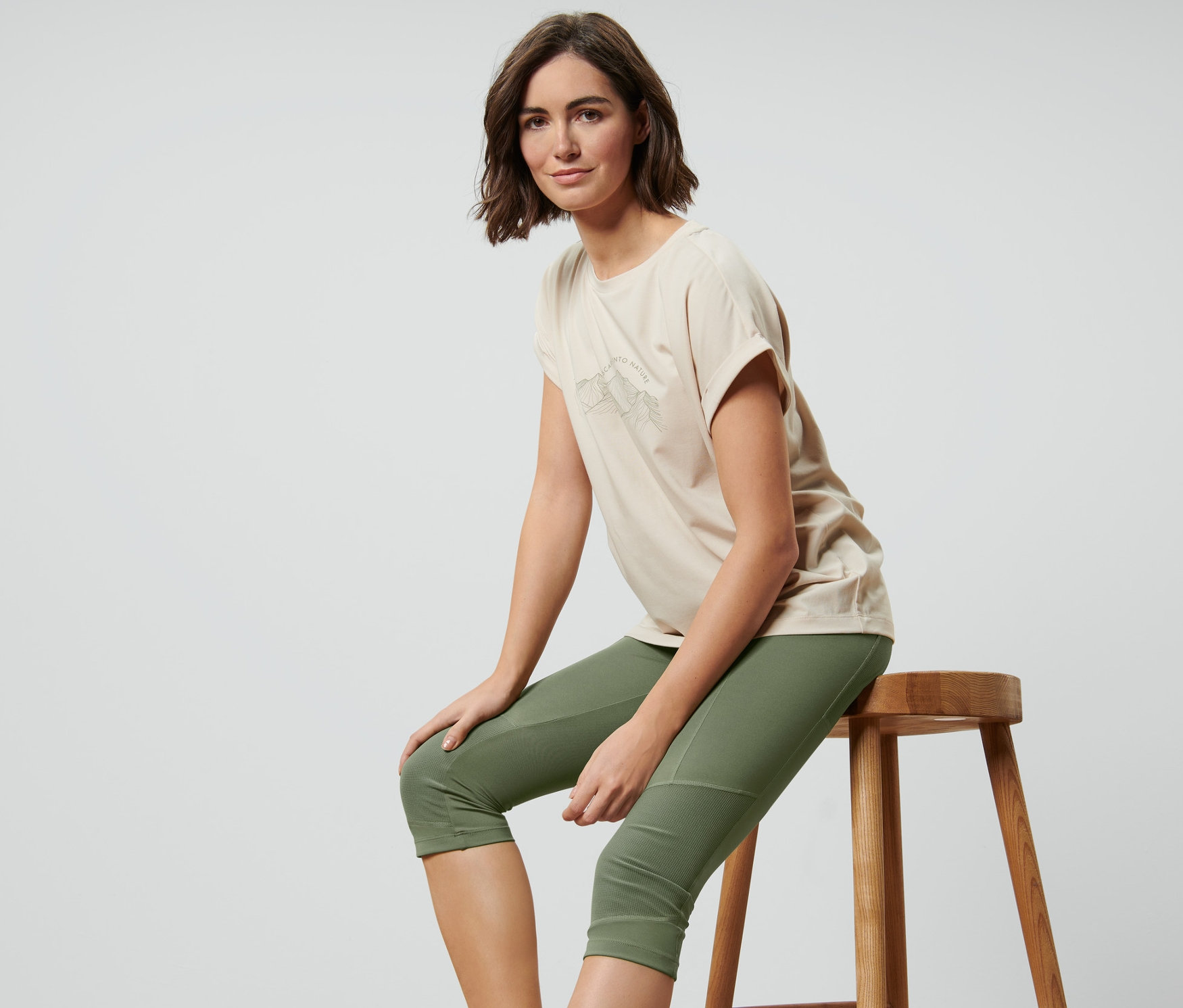Žena sedí na stoličke a má na sebe trojštvrťové trekingové legínsy, olivovozelené.