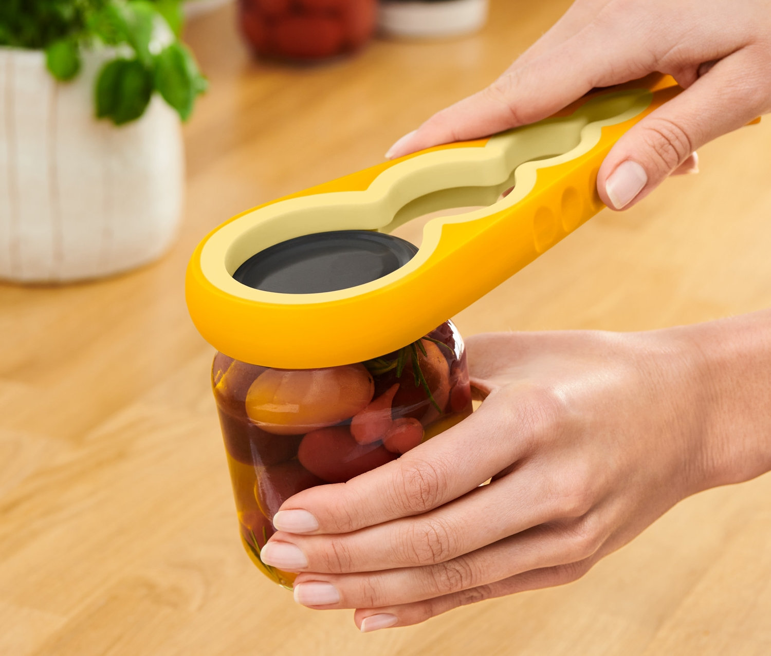 Žena otvára pohár s nakladanou zeleninou pomocou žlto-zeleného otvárača na poháre a fľaše.