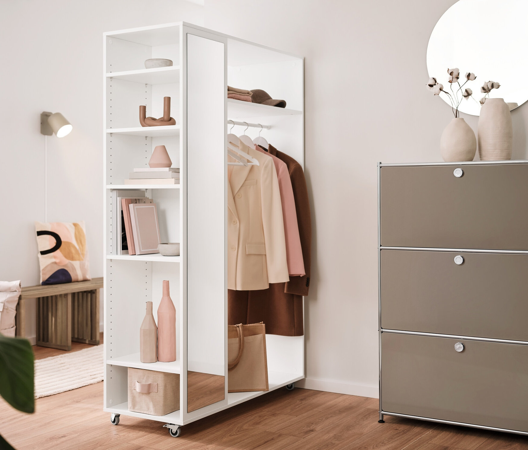 Interiér s rozkladacou lavicou, mobilnou vešiakovou skriňou so zrkadlovou skriňou, kovovým regálom »CN3« s 3 priehradkami a krémovou nástennou lampou z kovu.