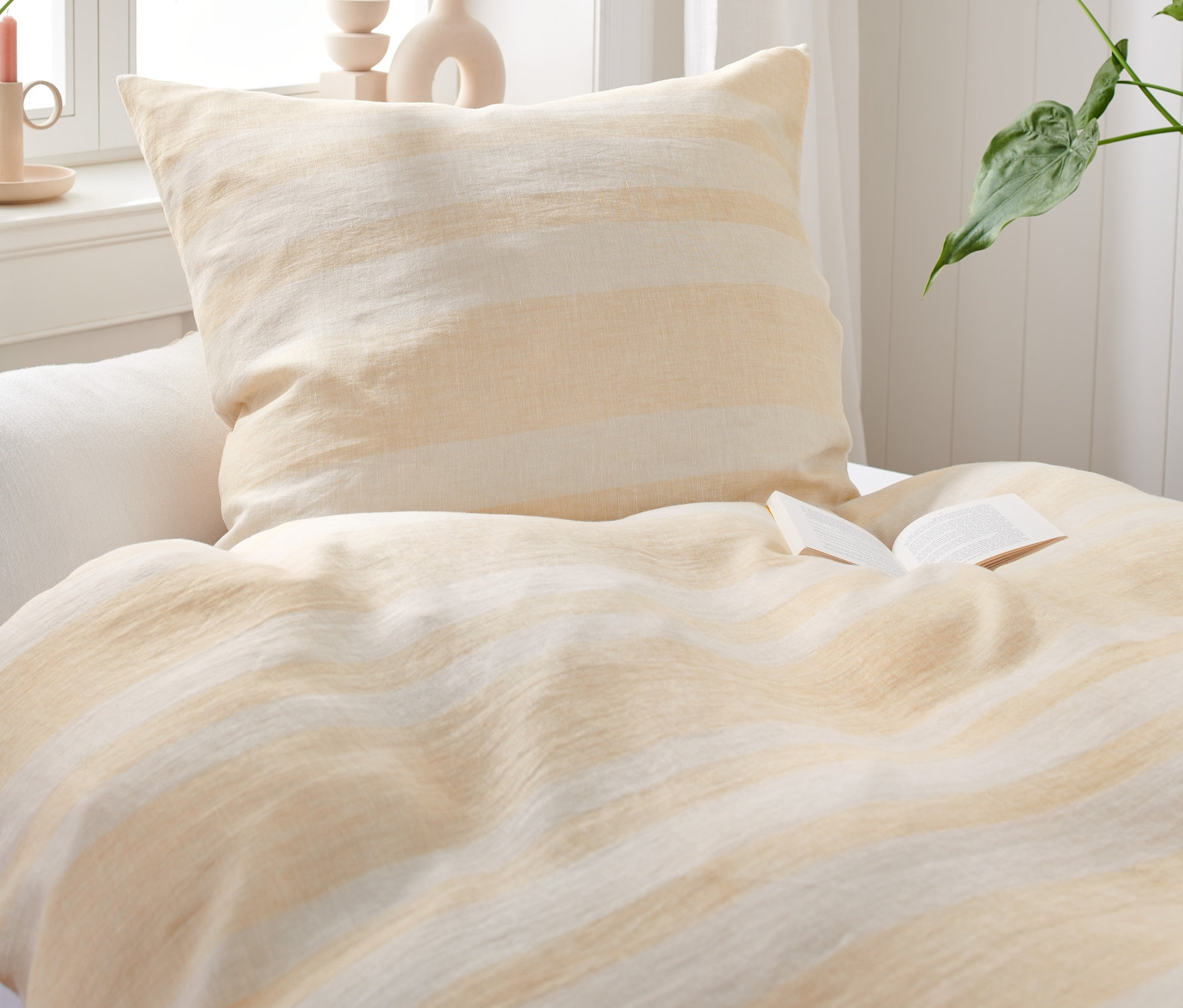 Detailný záber na posteľ s posteľnou bielizňou z praného ľanu a otvorenou knihou.