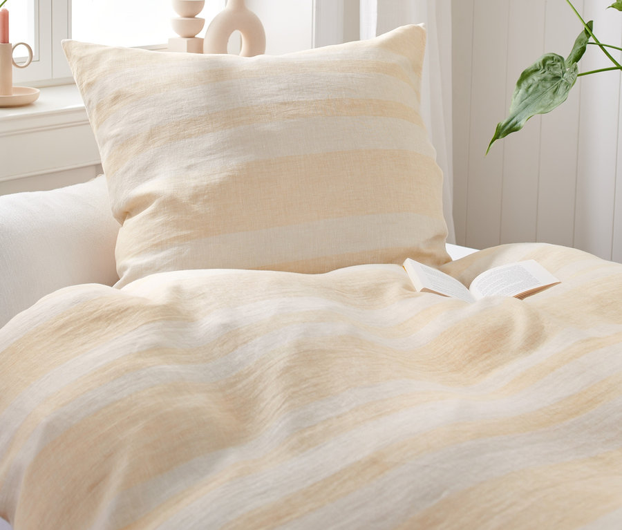 Detailný záber na posteľ s posteľnou bielizňou z praného ľanu a otvorenou knihou.