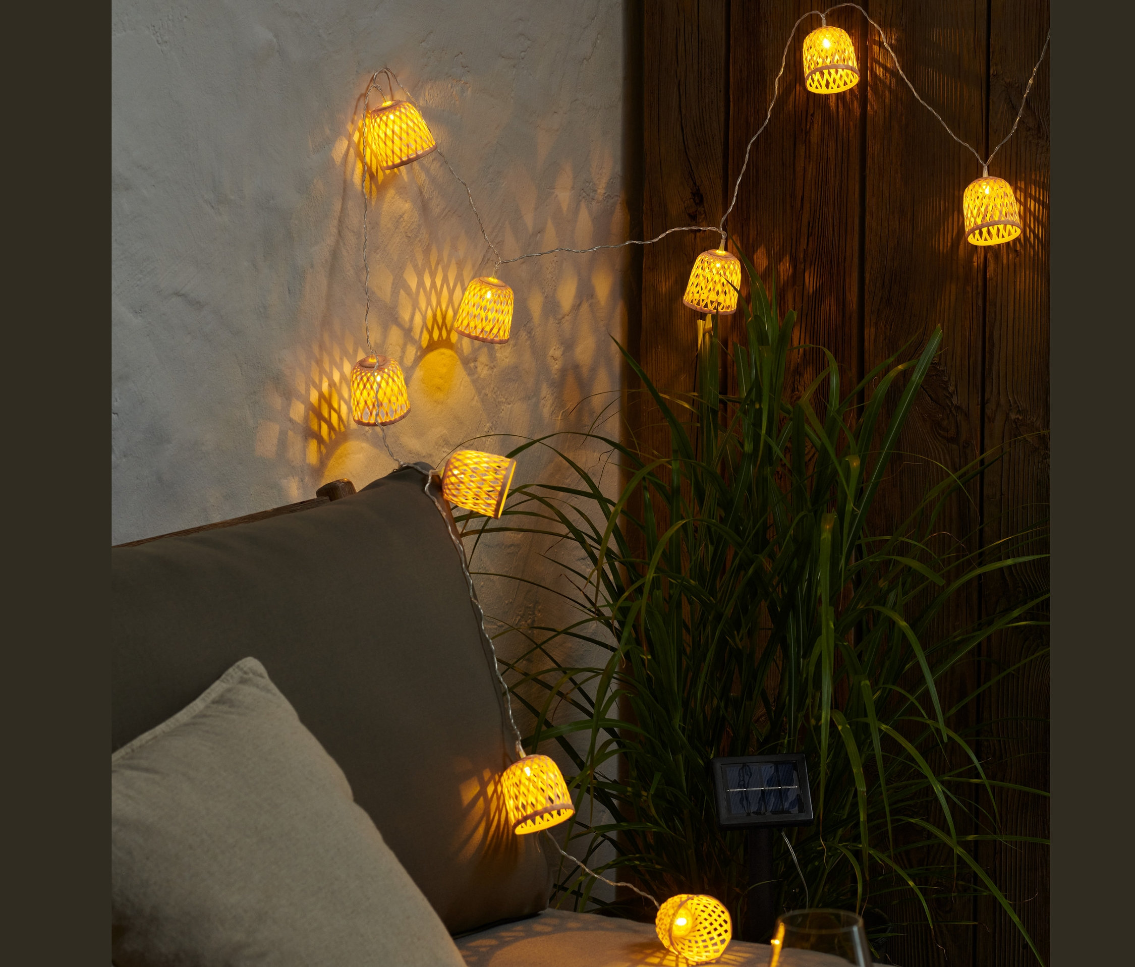 Svietiaca solárna svetelná reťaz s ozdobnými tienidlami visí nad sivou pohovkou.
