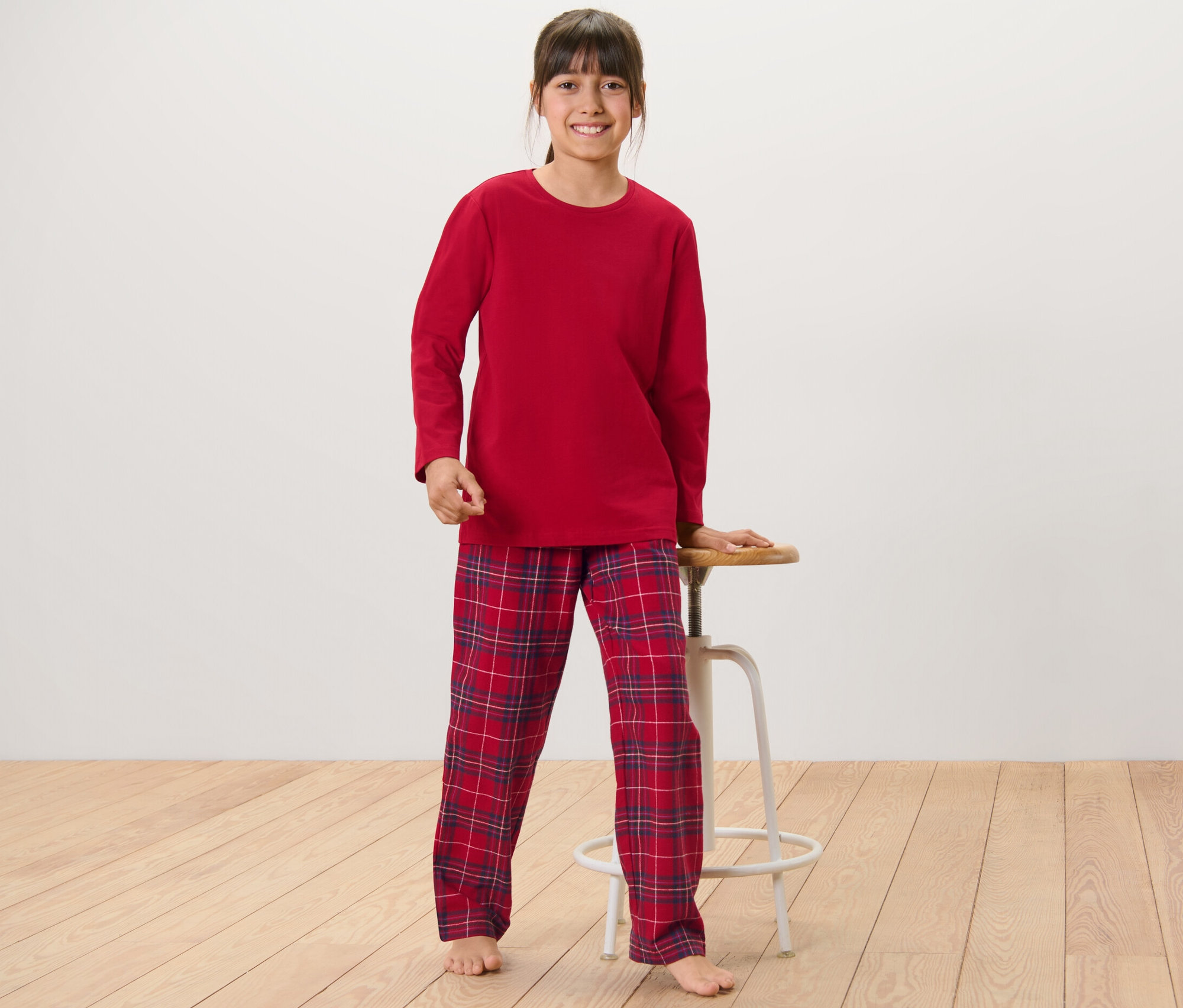 Dievča stojí a opiera sa o stoličku, má na sebe detské flanelové pyžamo.