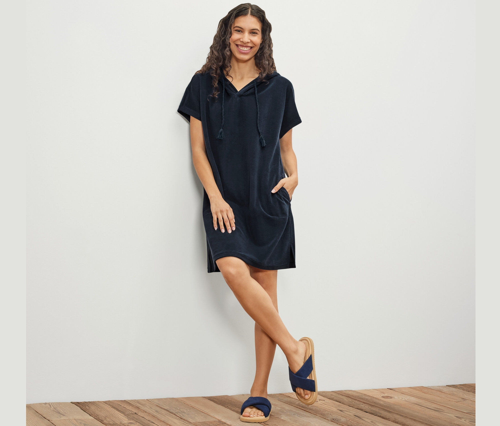 Žena pózuje opretá o stenu a má na sebe tmavomodré plážové froté šaty.