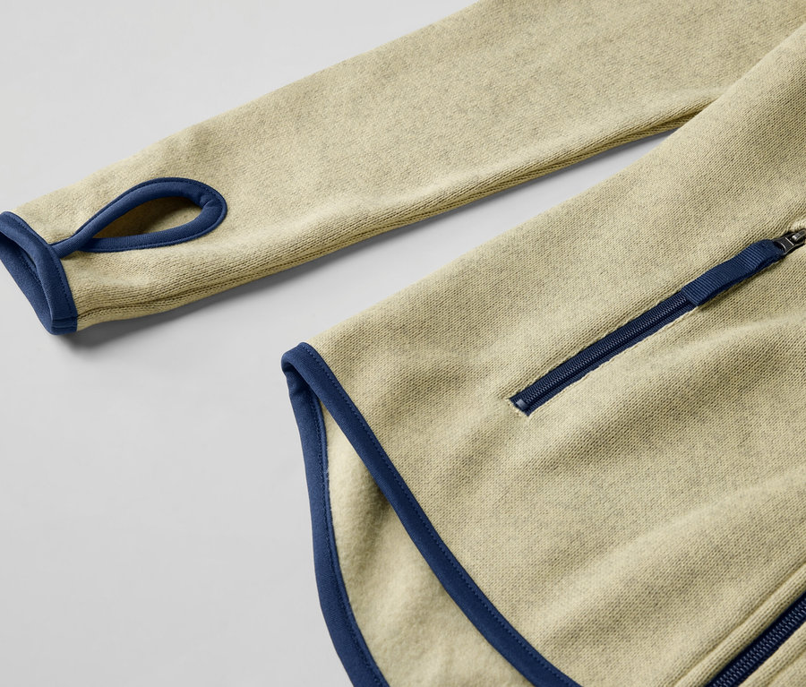 Detail žltej bundy z pleteného flaušu s modrými detailmi a zipsom.