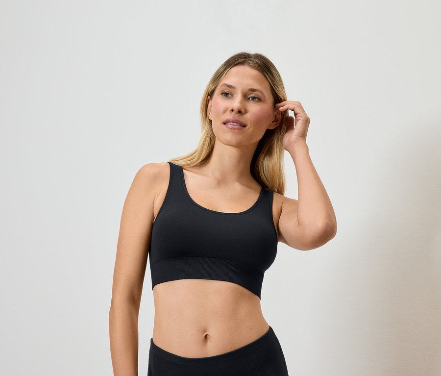 Blondínka v čiernej športovej podprsenke sa dotýka vlasov.