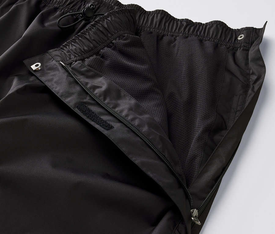 Detailný záber na čierne high-tech nohavice do dažďa s rozopnutým zipsom a viditeľnou sieťovanou podšívkou.