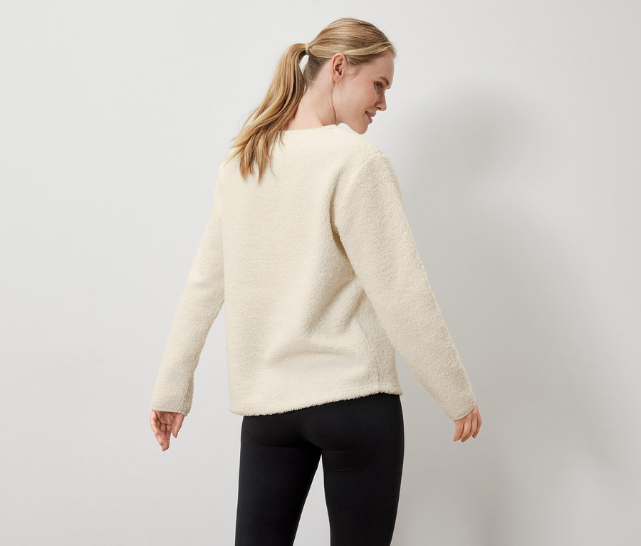 Žena má na sebe krémový sveter a čierne legíny.