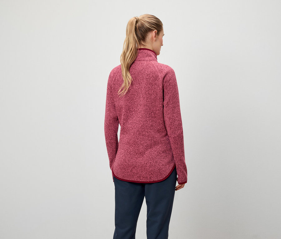 Zozadu je vidieť ženu s blond vlasmi stiahnutými do copu, má na sebe červenú mikinu a tmavomodré nohavice.