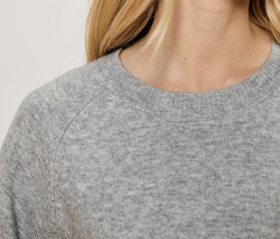 Detail dámskeho sivého svetra s okrúhlym výstrihom.