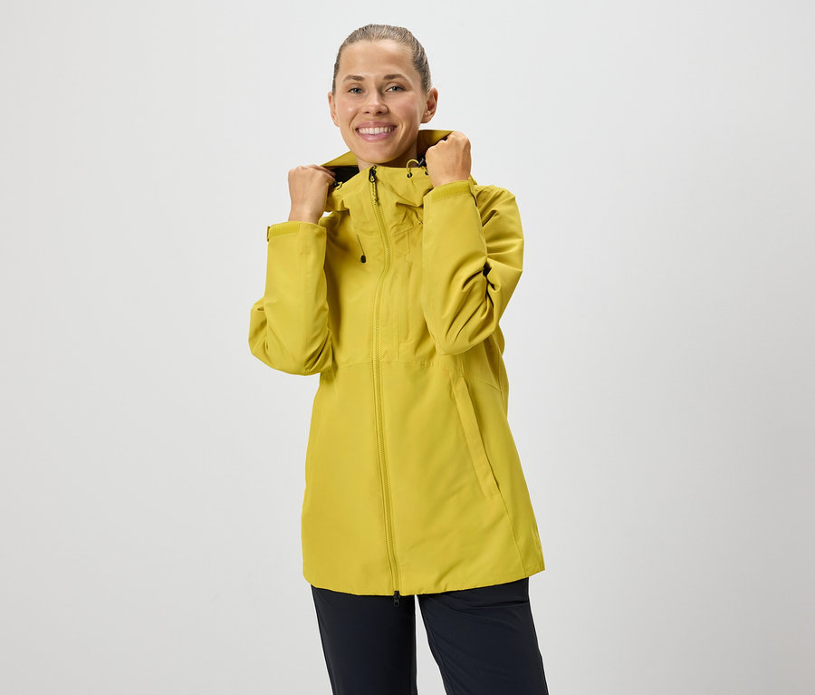 Žena si upravuje kapucňu žltej bundy na zips.