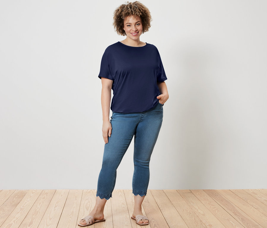 Žena pózuje v tmavomodrom blúzkovom tričku a sedemosminových tregínsoch s ažúrovou výšivkou.
