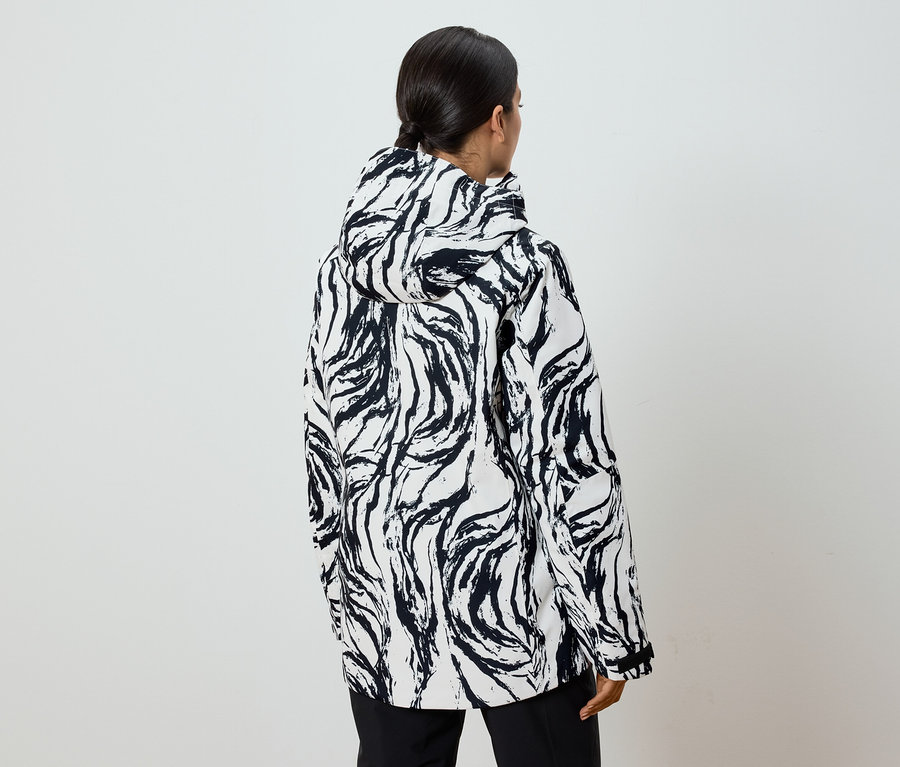 Zozadu je vidieť žena s copom v čierno-bielej bunde so vzorom a kapucňou.