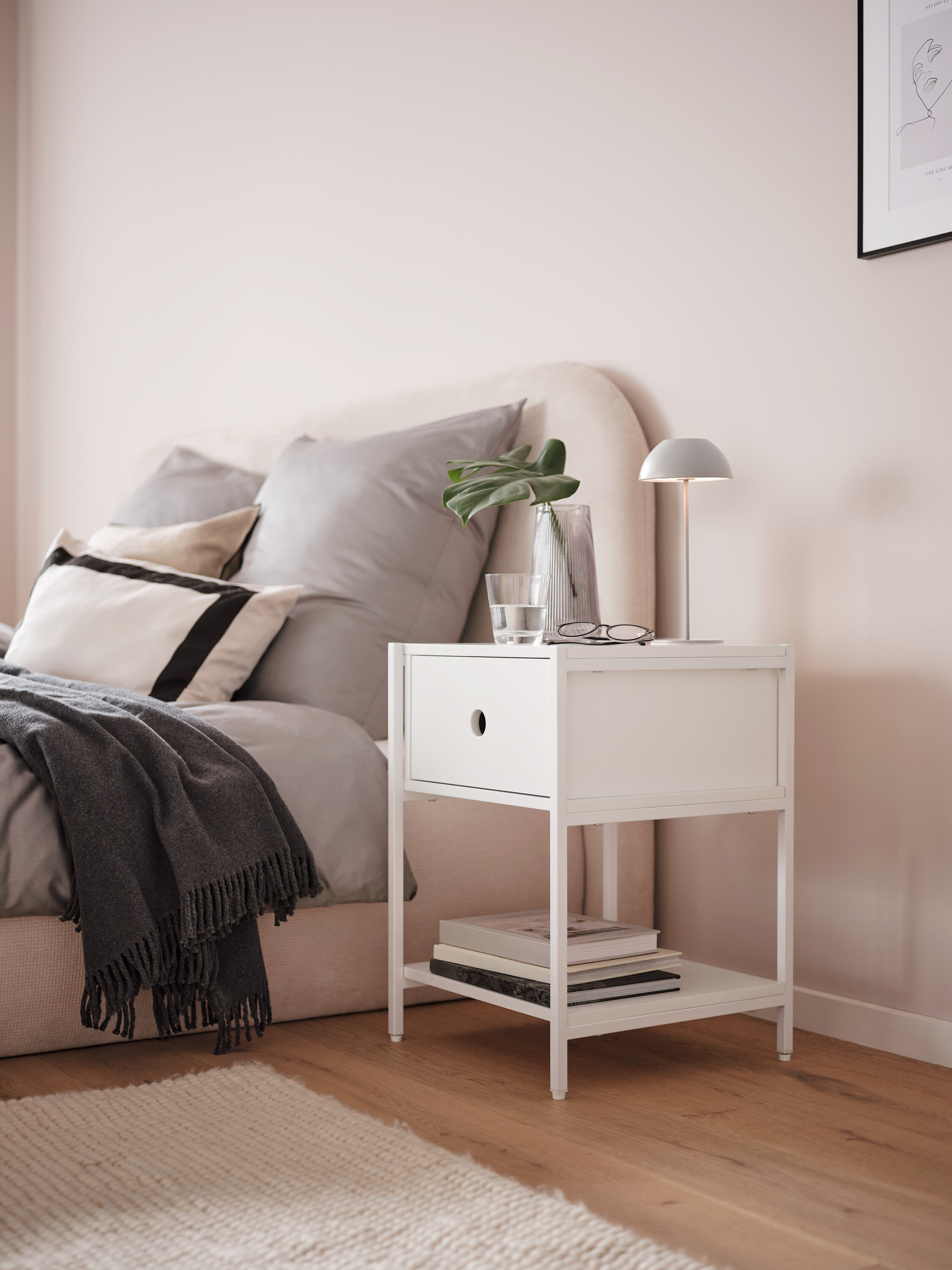 Sivá stolová LED lampa s akumulátorom na bielom nočnom stolíku vedľa postele.