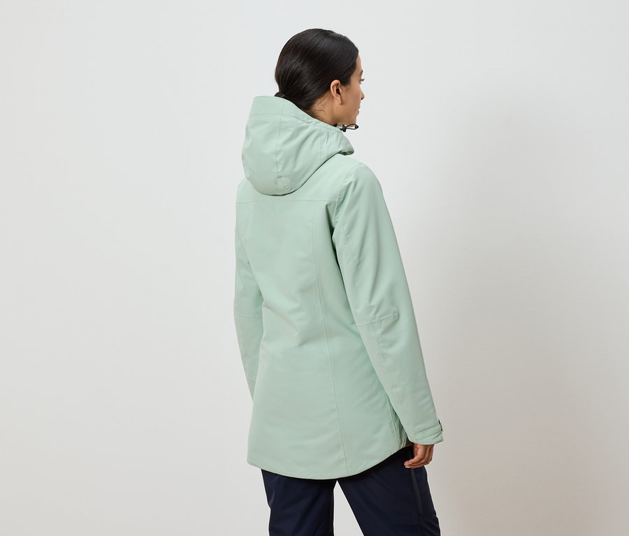 Pohľad zozadu na ženu v mätovo zelenej bunde s kapucňou a tmavomodrých nohaviciach.