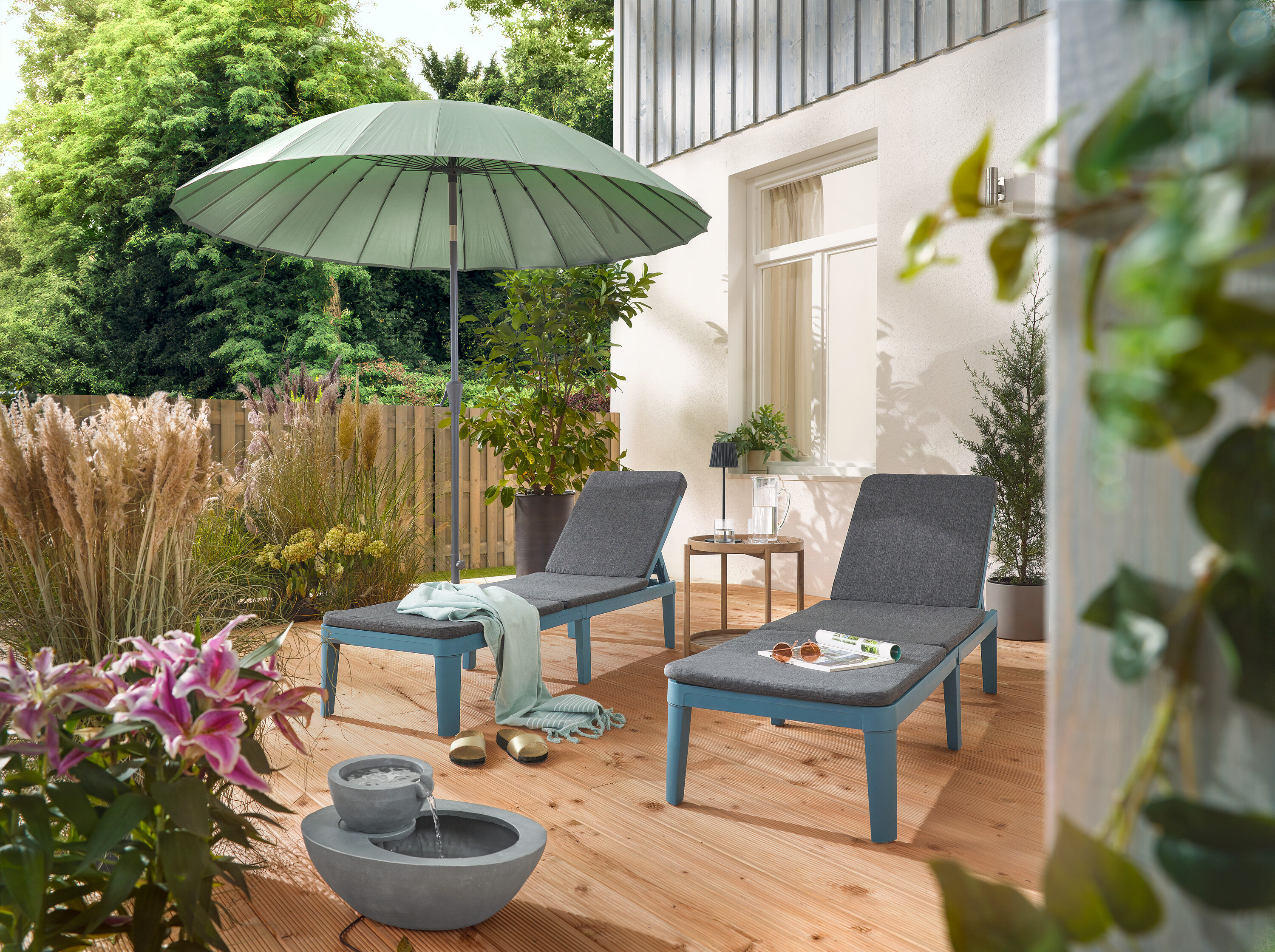 Na terase sú dve ležadlá pod svetlosivým slnečníkom Leco Shanghai a vedľa solárnej záhradnej fontány.