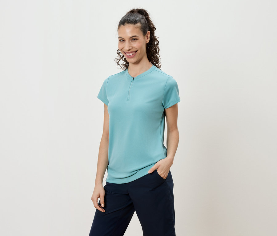 Žena s kučeravými vlasmi zopnutými do chvosta, má na sebe tyrkysové tričko a tmavomodré nohavice.