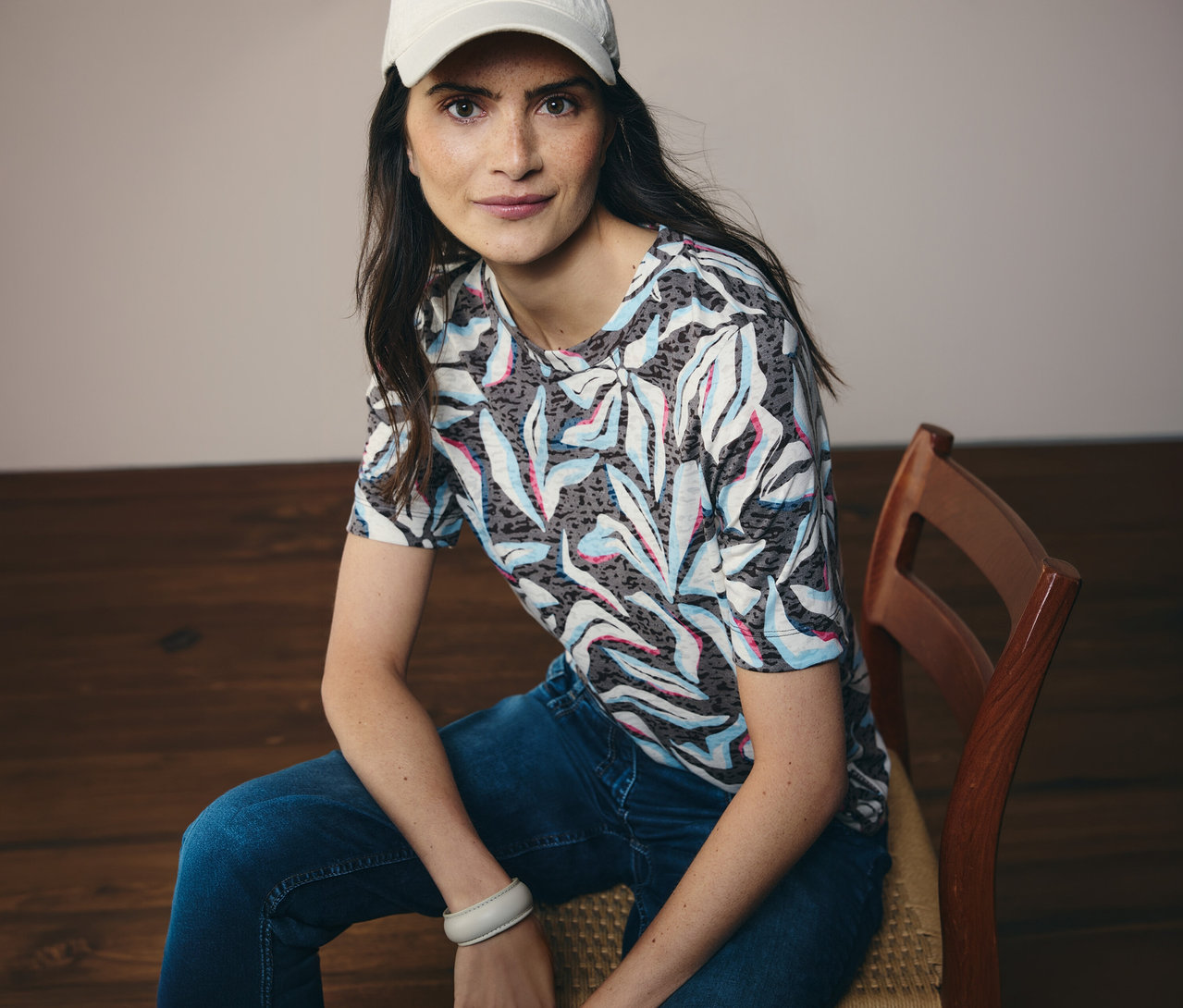 Žena v bielej čiapke sedí a má na sebe modré tričko s krátkym rukávom CECIL so vzorom.