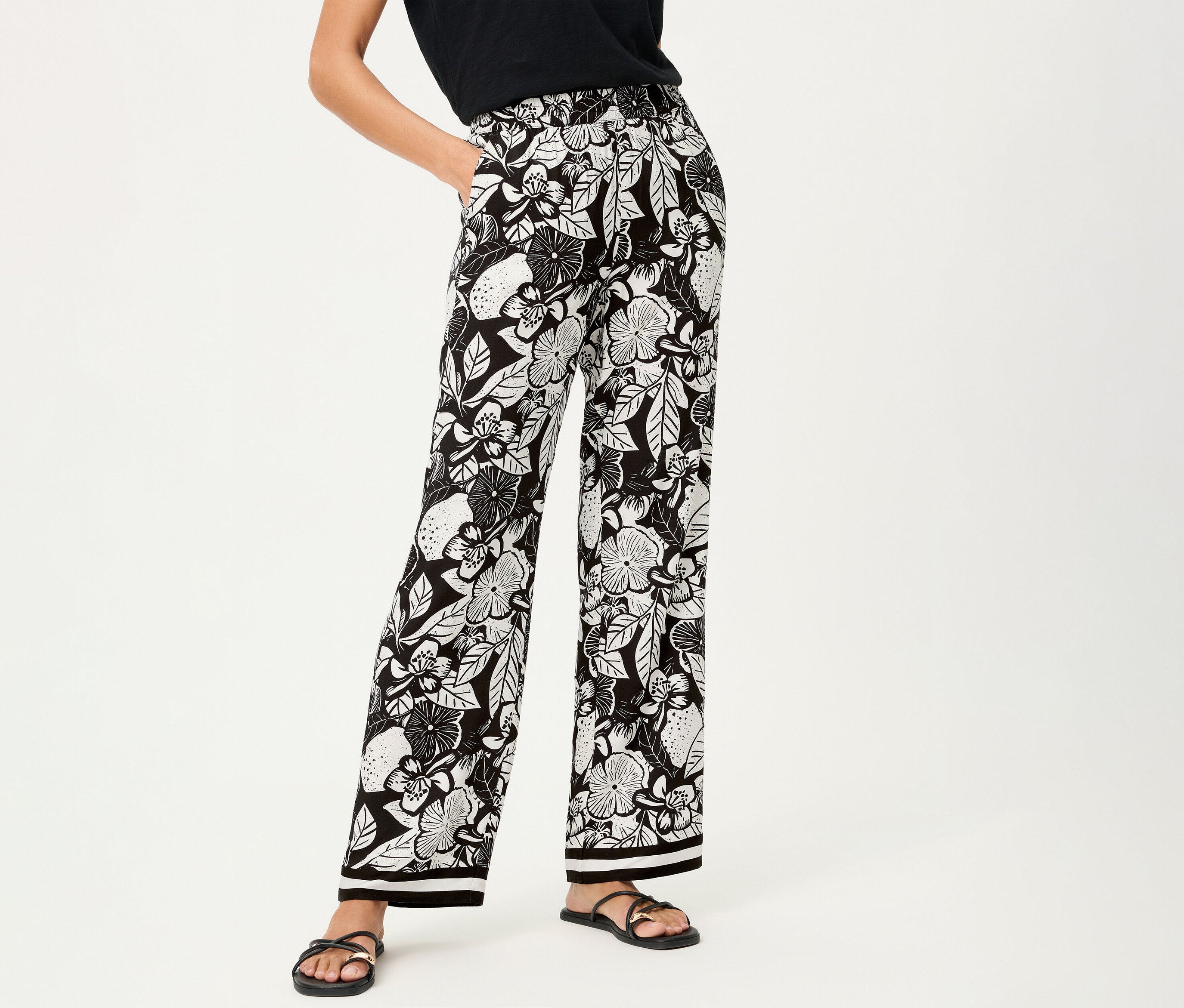 Žena má na sebe nohavice Olsen s kvetinovou potlačou a čierne sandále.
